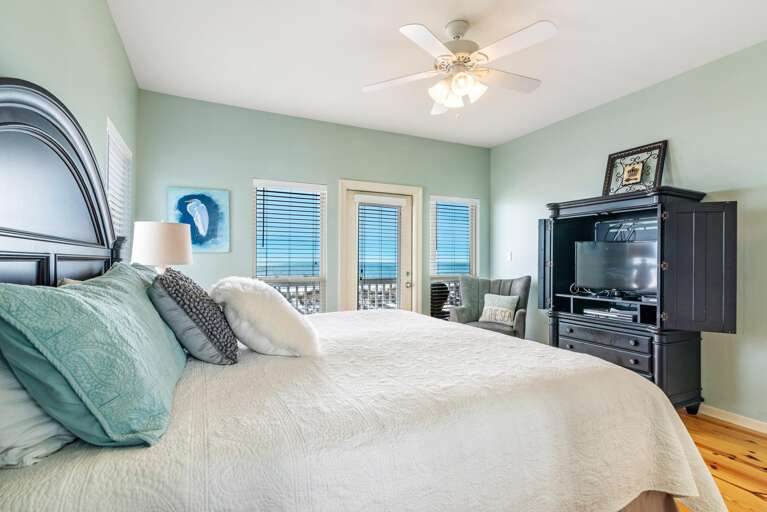 King bedroom with light green walls, white quilted bedding, dark wood armoire, and ocean views through glass door.