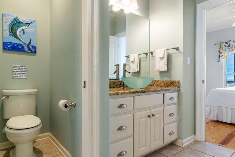 Separate toilet area with pale green walls and ocean-themed artwork above the toilet.