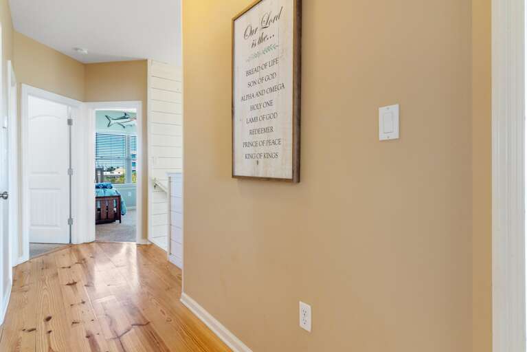 Hallway with polished wood floors leads to a bedroom featuring a dark wood bed and aqua walls with nautical decor.