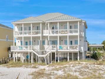 Elevated white coastal home with twin upper and lower wraparound porches featuring white railings and outdoor seating.