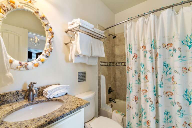 Tiled bathtub and shower surround with diamond-patterned accent strip, white shower curtain featuring coral and fish prints.