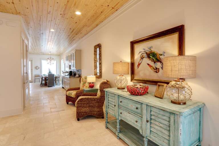 Wide view of the living area shows natural stone tile flooring, a pine-plank ceiling, and a coastal-themed blue distressed sideboard.