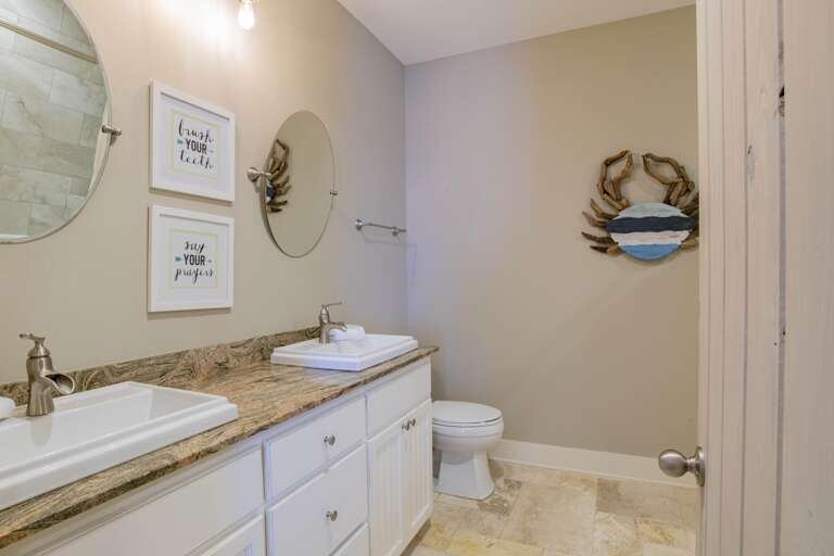 Bathroom with dual rectangular sinks set in granite countertop, round mirrors, and beige tile flooring.