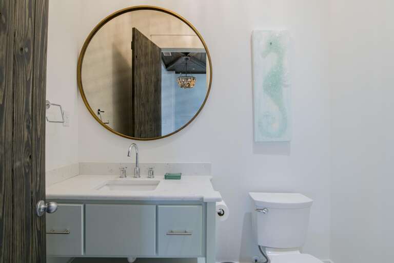 Powder room with pale blue vanity, white quartz countertop, round brass-framed mirror, and seahorse wall art.