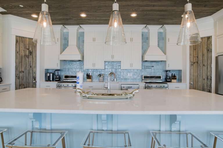 Quartz island with silver tray and clear acrylic bar stools beneath wood-plank ceiling in the kitchen.
