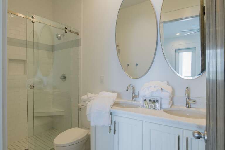 Bathroom with dual oval mirrors above white quartz countertops and a glass-enclosed shower featuring subway tile.