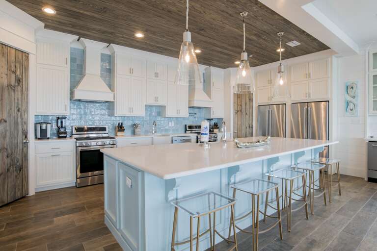 Blue island with white marble countertop and five clear acrylic stools beneath wood-plank ceiling.