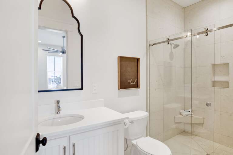 Bathroom features a white vanity with round sink, arched black-framed mirror, and glass-enclosed marble shower with corner bench.