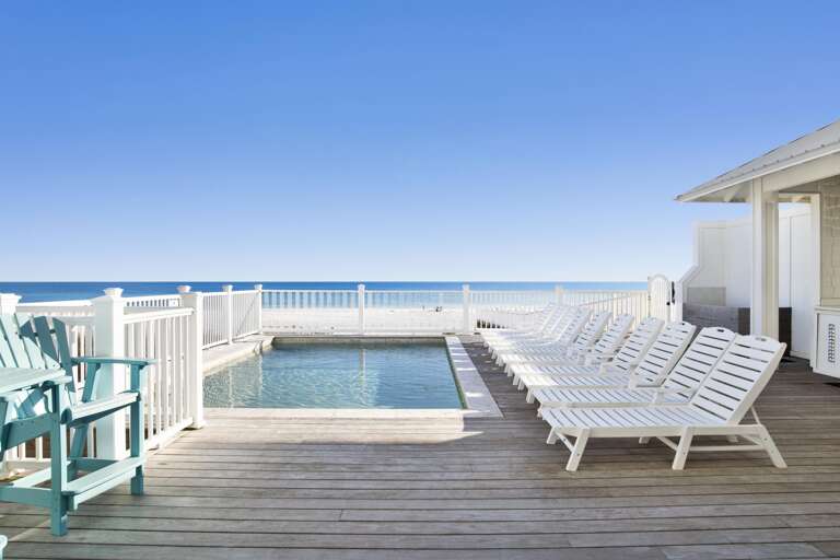 Oceanfront deck with white slatted lounge chairs, turquoise Adirondack chairs, and a rectangular plunge pool.