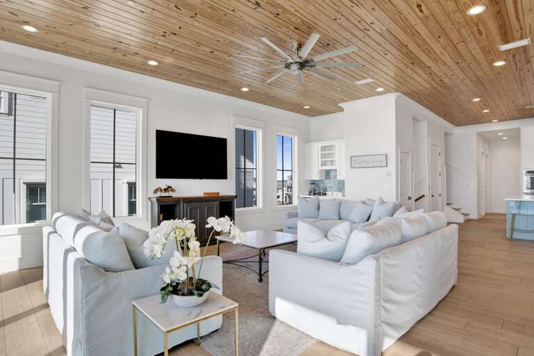 Three large windows flank a flat-screen TV above a dark wood console in the bright living room.