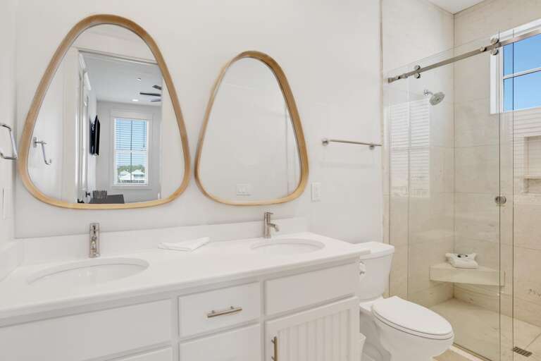 Bathroom features a double vanity with white quartz countertop, oval wood-framed mirrors, and a glass-enclosed tiled shower.