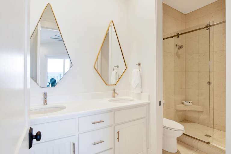 Bathroom featuring dual diamond-shaped mirrors above white quartz countertops and a glass-enclosed tiled shower with built-in bench.