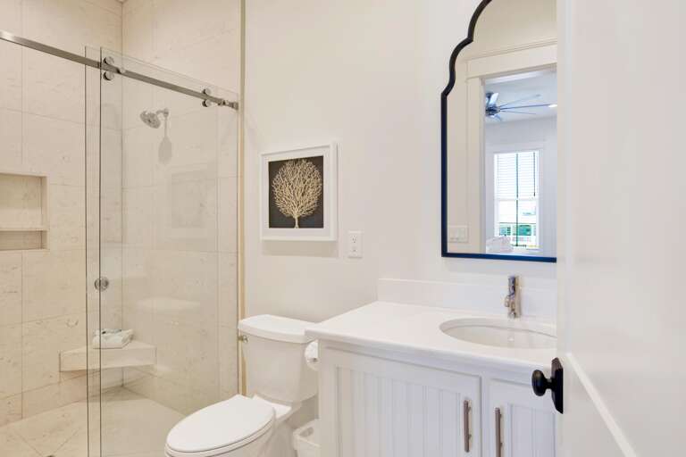 Bathroom with glass sliding shower door, marble tile walls, white vanity, and framed coral artwork.