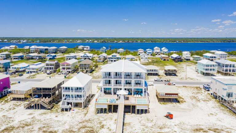 Two connected white beachfront homes with metal roofs, spacious balconies, and twin pools facing the sandy shore.