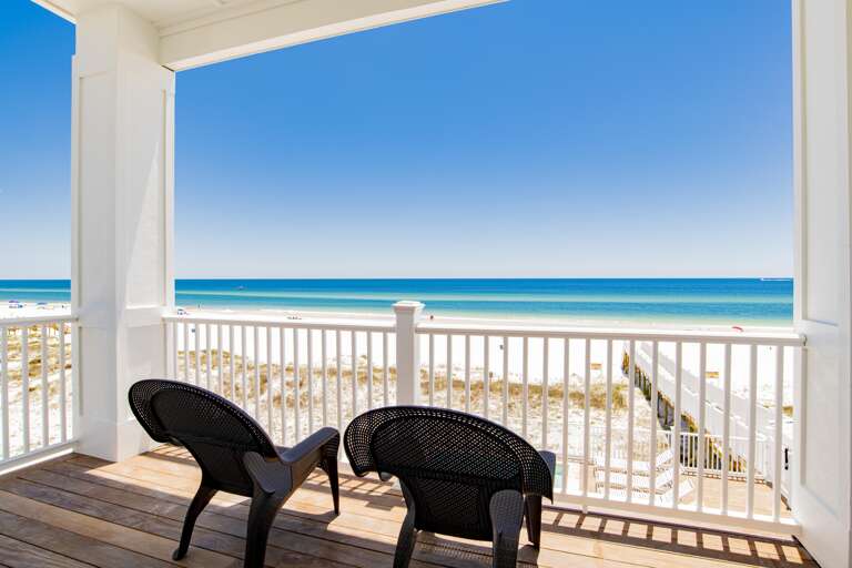 Covered balcony with dark woven chairs overlooks white sand dunes and turquoise Gulf waters.