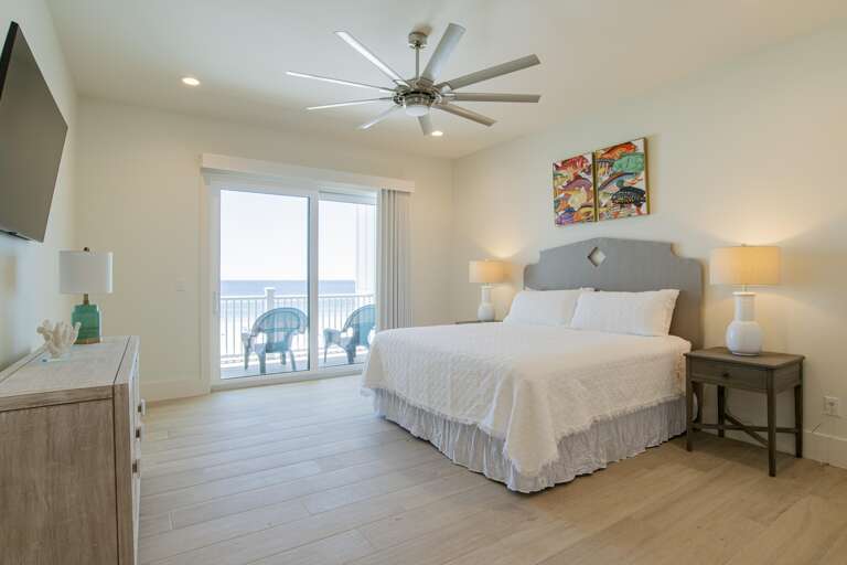 Bedroom with king bed, wood-look tile flooring, sliding glass doors opening to balcony with ocean view.