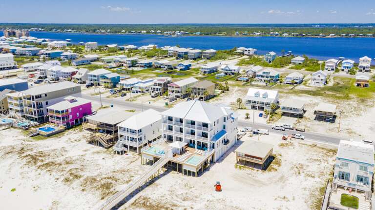Dual beachfront homes with spacious balconies, metal roofs, and two elevated pools overlooking white sand and turquoise Gulf waters.