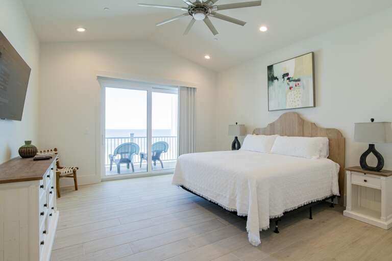 King bed with scalloped wood headboard faces sliding glass doors opening to balcony with ocean view.