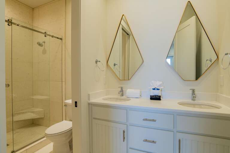 Bathroom features white double vanity with diamond-shaped mirrors and a glass-enclosed shower with built-in bench.