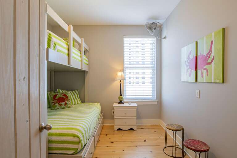 Bunk beds with green-striped bedding and crab-themed pillows sit beside a white nightstand and window with blinds.