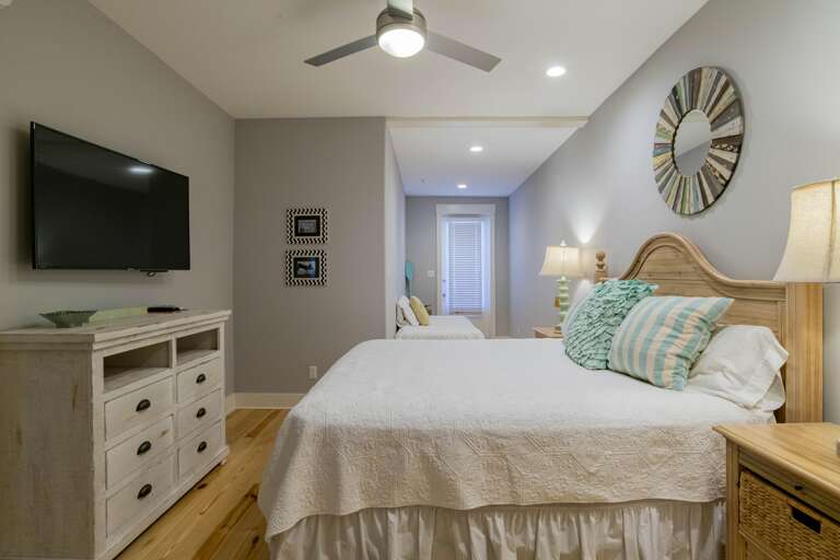 Two beds with wooden headboards and white quilted bedding are arranged along polished pine floors beneath recessed lights.