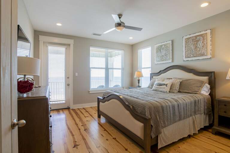 Bedroom with wood-framed upholstered bed, hardwood floors, dresser, and balcony access through glass door.