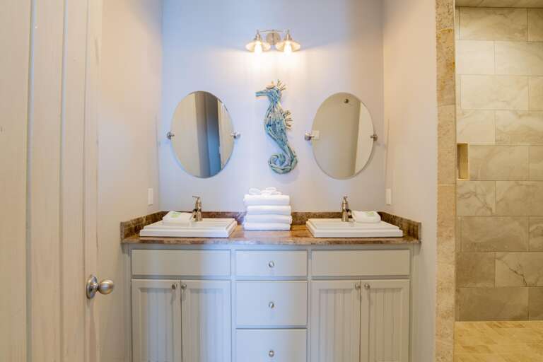 Dual rectangular sinks with brushed nickel faucets sit on a granite countertop beneath two oval mirrors and a seahorse wall decoration.