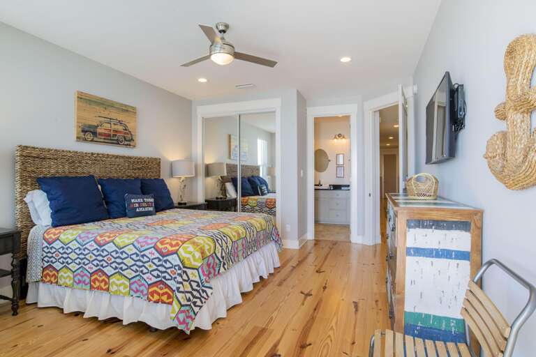 Polished pine floors stretch beneath a colorful patterned quilt and woven headboard in the bedroom.