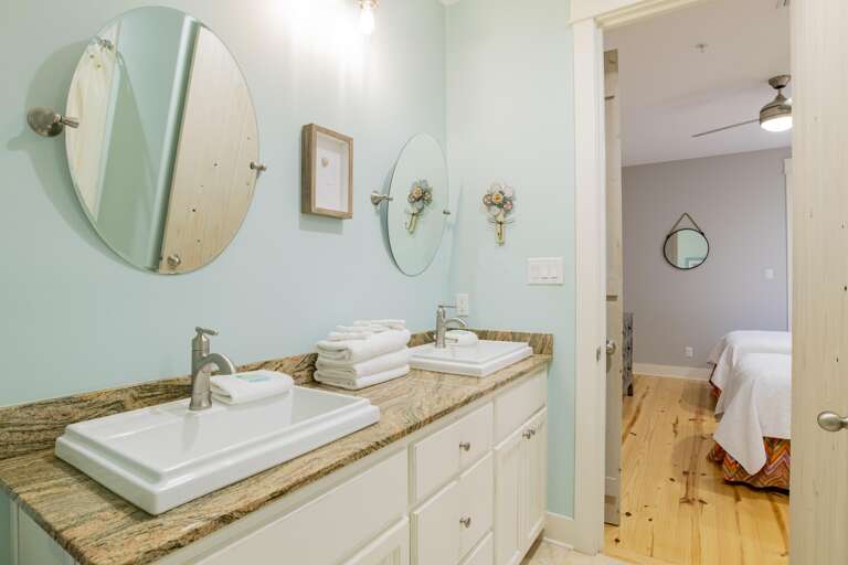 Dual rectangular sinks with brushed nickel faucets sit on a granite countertop beneath round mirrors in a light blue bathroom.