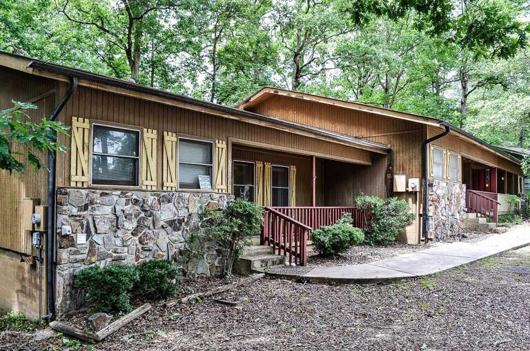 A charming row of rustic wooden cabins nestled among tall green trees, each with its own stone foundation and welcoming covered porchâperfectly secluded for a peaceful wooded retreat.