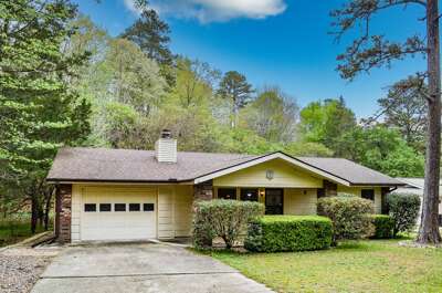Charming single-story ranch-style home surrounded by mature trees and lush landscaping, offering a peaceful retreat in a wooded residential area.