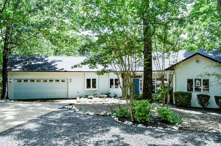 A beautiful vacation home nestled among towering trees, with lush landscaping and a circular gravel drive welcoming your arrival to this peaceful wooded retreat.