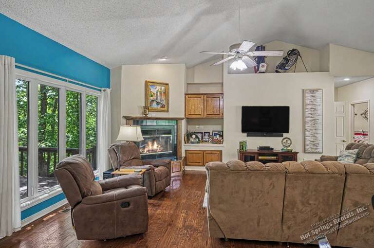 Relax in your spacious living room with comfortable seating, a cozy fireplace, and large windows framing the natural wooded surroundings outside.
