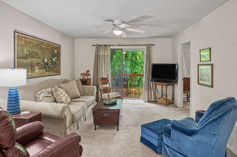 Relax in your comfortable living room with plush seating and natural light streaming through the door to your private balcony, where lush greenery awaits.