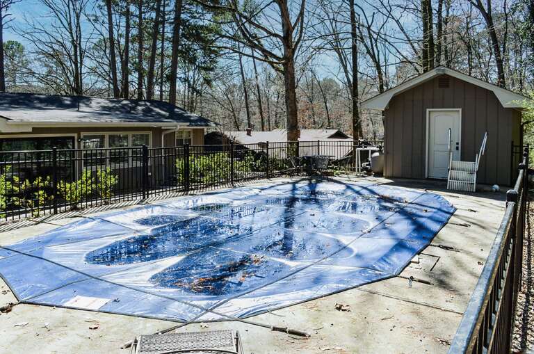 Private pool area surrounded by wooded landscape, complete with safety fencing and pool house for seasonal relaxation.