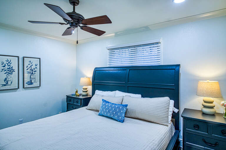 Drift off peacefully in your stylish bedroom featuring a comfy queen bed, soothing coastal decor, and gentle ceiling fan for the perfect night's sleep.