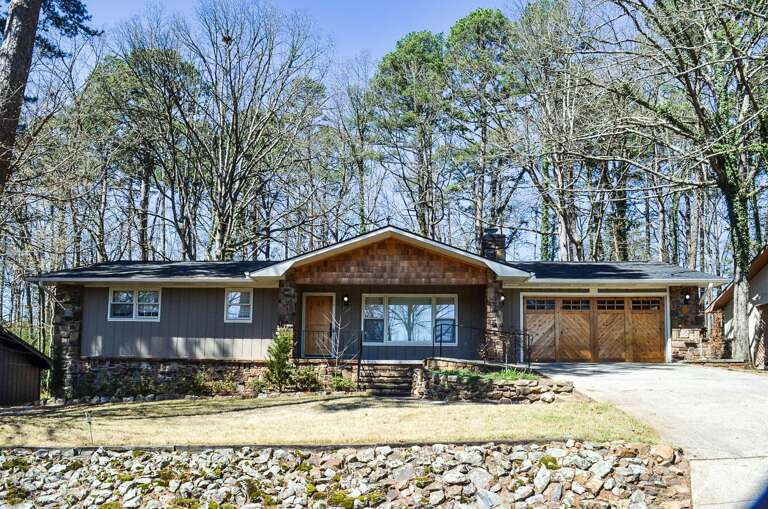A charming ranch-style home nestled among mature trees with stone accents and a welcoming front porch.
