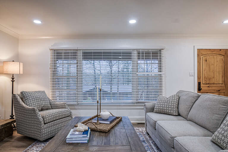 Sink into plush seating where natural light filters through blinds, creating your perfect space to unwind with a book.