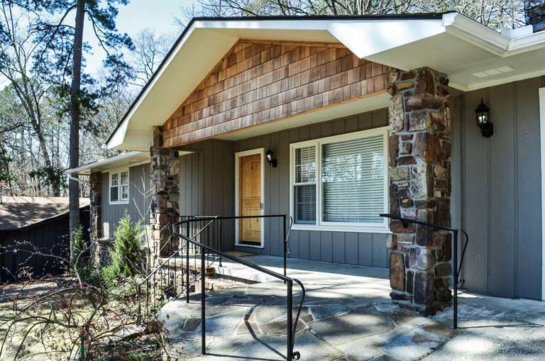 A welcoming property entrance featuring natural stone columns and wood shingle accents, nestled among mature trees in a peaceful residential setting.