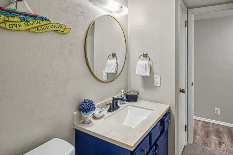 Your bathroom features a crisp white vanity with a modern navy-blue cabinet, fresh towels, and a stylish gold-framed mirror that brightens the space.
