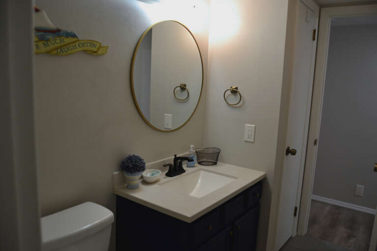 Freshen up in your clean, thoughtfully styled bathroom with a brass-framed mirror, navy vanity, and charming coastal accents that make daily routines feel special.