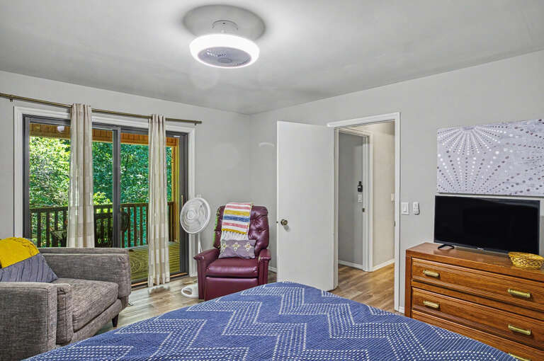 Relax in your serene bedroom with garden views through sliding glass doors, a cozy seating nook, and modern ceiling fan to keep you comfortable.