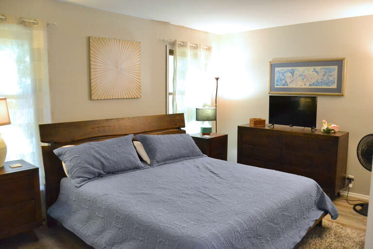 Unwind in your serene bedroom featuring a plush king bed, elegant artwork, and modern entertainment. Natural light filters through soft curtains while dark wood furnishings create a cozy, sophisticated retreat for restful nights.