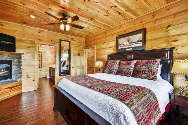 Large bed on ornate bedframe by a fireplace and wall-mounted TV in a bedroom.