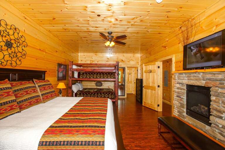 A TV sits above a fireplace in front of a full bed and a bunk-bed.