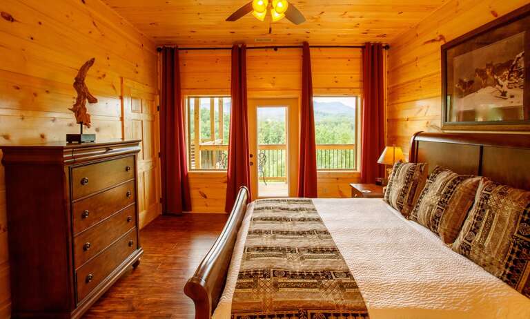 Bedroom with Large Bed, Dresser, Nightstand, Lamp, and Window Door to the Balcony.