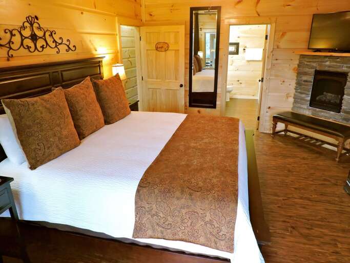 Bedroom with Large Bed, Nightstand, Lamp, Bench, and Fireplace.