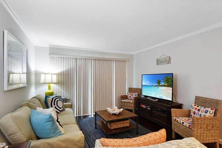 Living Room With Beige Sofa, Brown Coffee Table, TV, And Light Through Sheer Curtains