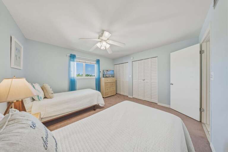 Crisp white bedding, soft neutral carpeting, and light blue accents create a bright and inviting guest retreat.