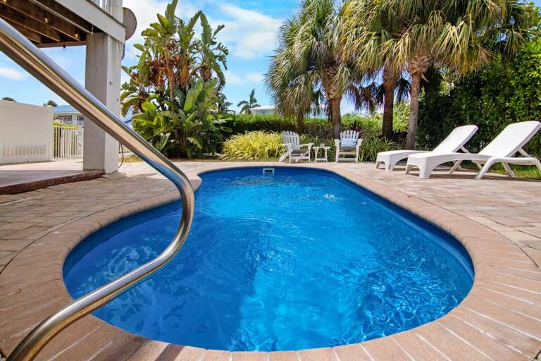 Cool off in a private backyard pool surrounded by tropical landscaping, lounge chairs, and a sunny Florida Keys patio.